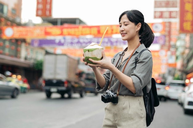 Happy young Asian woman backpack traveler drinking a coconut juice at China town street food market in Bangkok Thailand Traveler checking out side streets