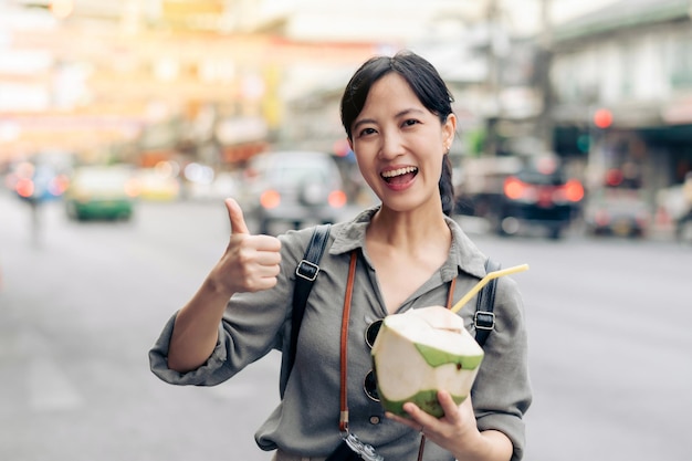 Happy young Asian woman backpack traveler drinking a coconut juice at China town street food market in Bangkok Thailand Traveler checking out side streets