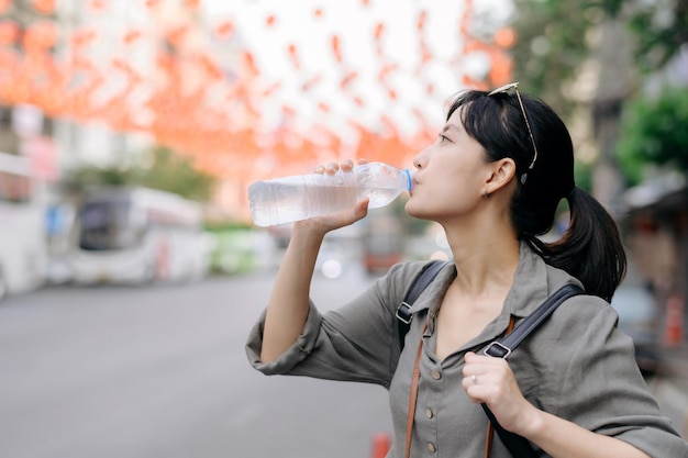 Happy young Asian woman backpack traveler drinking a cold water at China town street food market in Bangkok Thailand Traveler checking out side streets