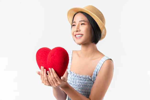 Happy young Asian woman in a blue dress holding red hearts and smiling on white background