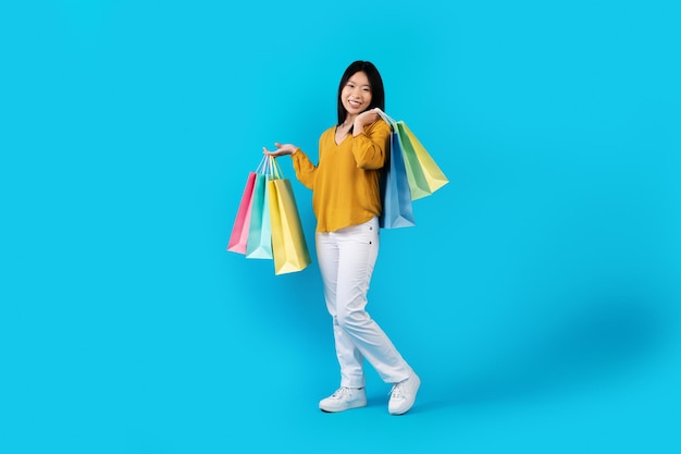 Happy young asian woman carrying colorful shopping bags