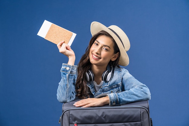 Happy young Asian woman holding passport with boarding pass and presenting on blue color