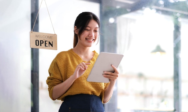 Happy young Asian woman owner standing holding a tablet with open sign board