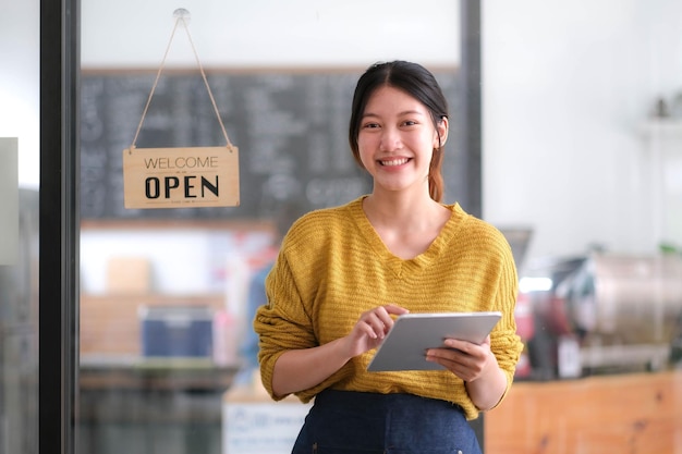 Happy young Asian woman owner standing holding a tablet with open sign board