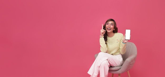 Happy young Asian woman sitting on sofa feeling happiness and gesture showing mobile smartphone