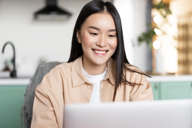 Happy young asian woman working with laptop from home girl using computer to work study online from ...