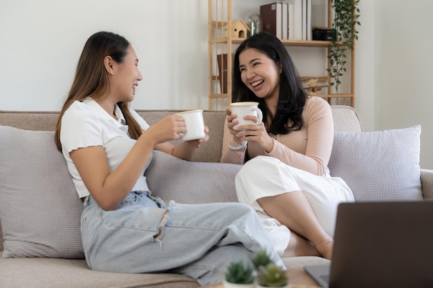 Happy young asian women LGBT lesbian happy couple sitting on sofa using laptop a computer in living room at home LGBT lesbian couple together