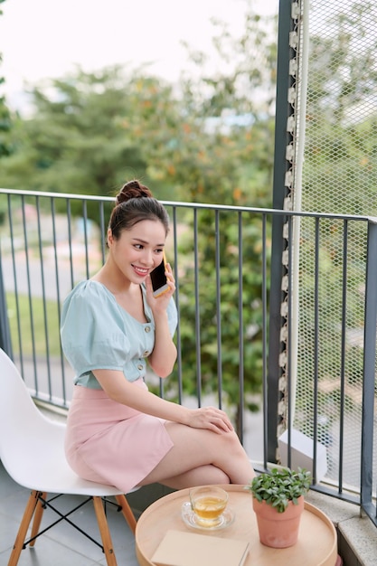 Happy young Asian womna using phone when sitting drink tea at the balcony