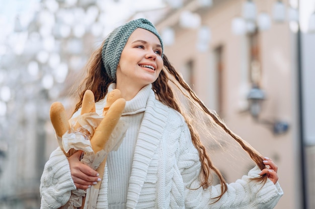 A happy young and attractive beauty with long hair smiles brightly and touches a lock of hair. Holding a few loaves in your hand. Advertising campaign of bakery products. Space for text or logo.