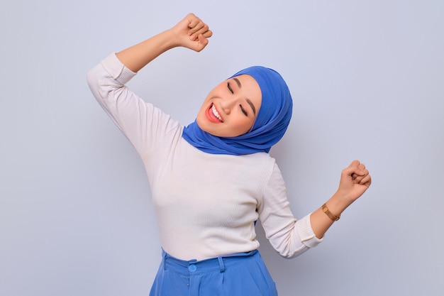 Happy young beautiful Asian Muslim woman dancing to her favorite music forgetting about all problems isolated over white background