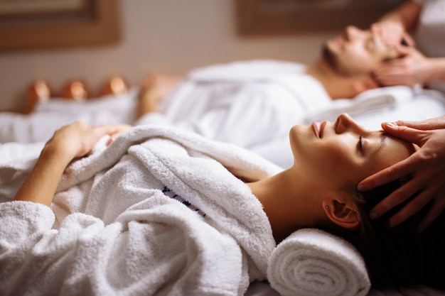 Happy young beautiful couple enjoying head massage at the spa