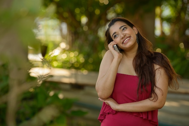 Happy young beautiful Indian woman talking on the phone at the park