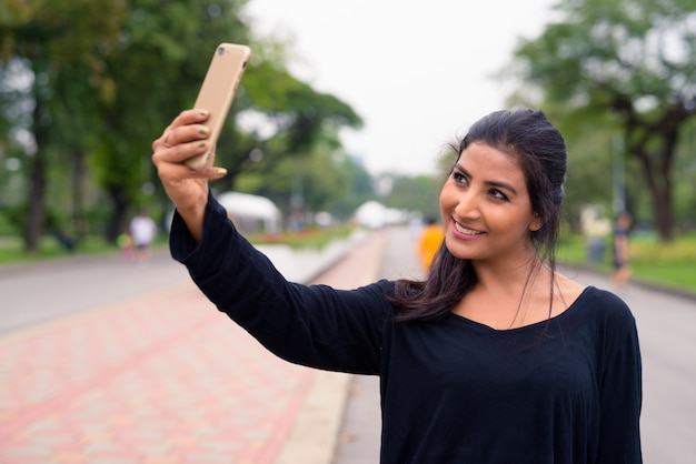 Photo happy young beautiful persian woman taking selfie at the park