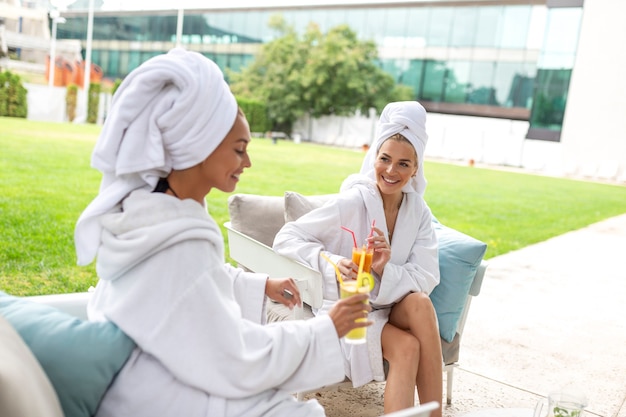 Happy young beautiful women enjoying fun time after spa procedures together in luxury hotel, wearing towels on heads and bathrobes.