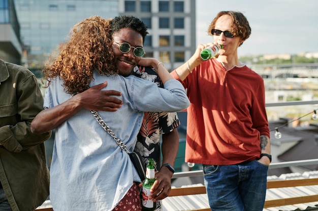 Happy young black man with bottle of beer embracing adolescent girl