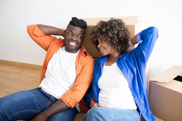 Happy young black spouses relaxing on floor after moving home