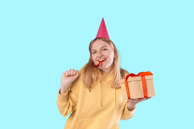 Happy young blonde woman 20s wears green denim jacket hold shake red present box with gift ribbon bow try to guess what inside isolated on plain pastel light beige background studio portrait