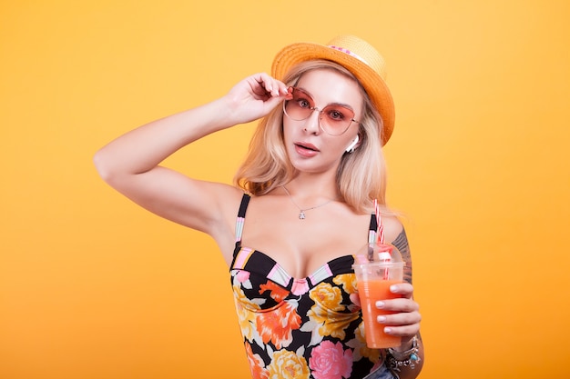 Happy young blonde woman holding fresh orange juice in studio