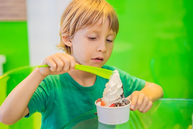 Happy young boy eating a tasty ice cream or frozen yogurt