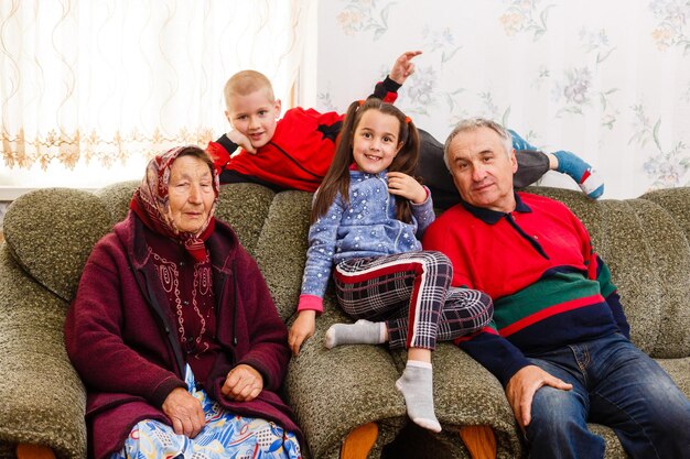 Happy young boy and girl with their laughing grandparents smiling at the camera as they pose together indoors