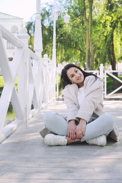 Happy young brunette woman outdoor dressed in faux white fur coat and jeans