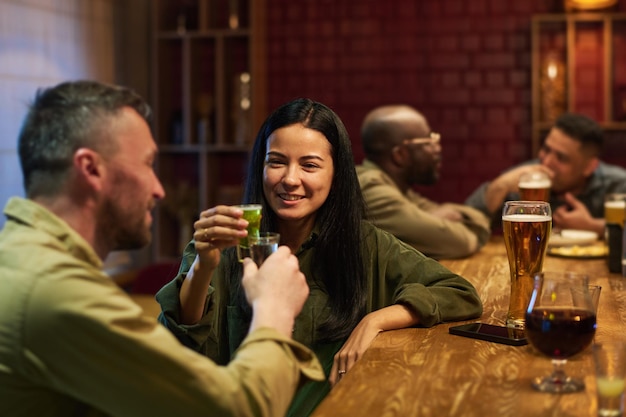 Happy young brunette woman with glass of aperitif toasting with her boyfriend