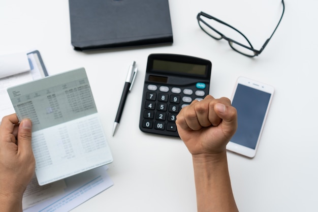 Happy Young Business man holding saving account passbook on white desk at home