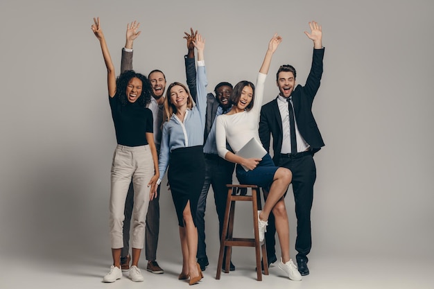 Happy young business team in formalwear gesturing while standing on beige background