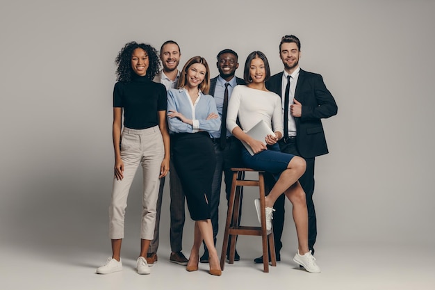 Happy young business team in formalwear looking at camera while standing on beige background