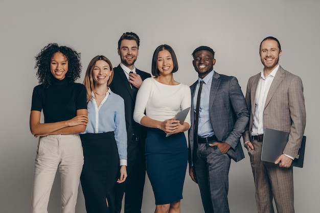 Happy young business team in formalwear looking at camera while standing on beige background