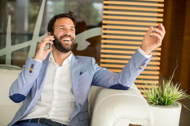 Happy young businessman sitting in office and using mobile phone