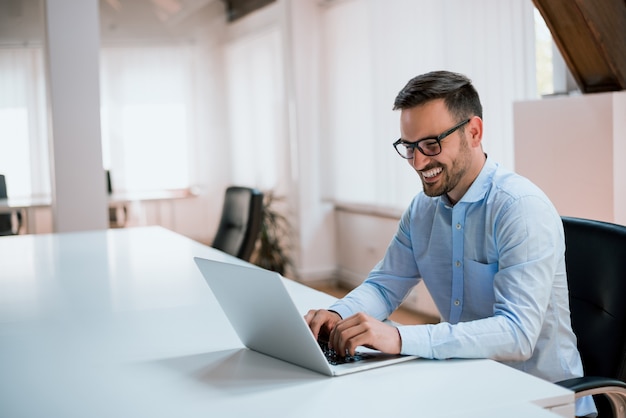 Happy young businessman using laptop at his office desk.