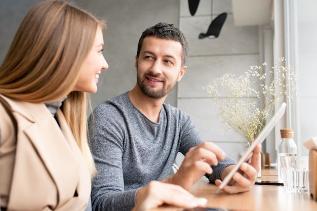 Happy young businessman with tablet and his pretty colleague consulting about working points while planning work at meeting