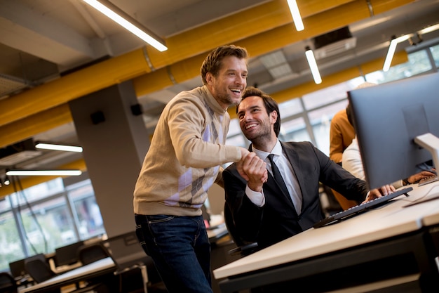 Happy young businessmen handshaking by the table in the office