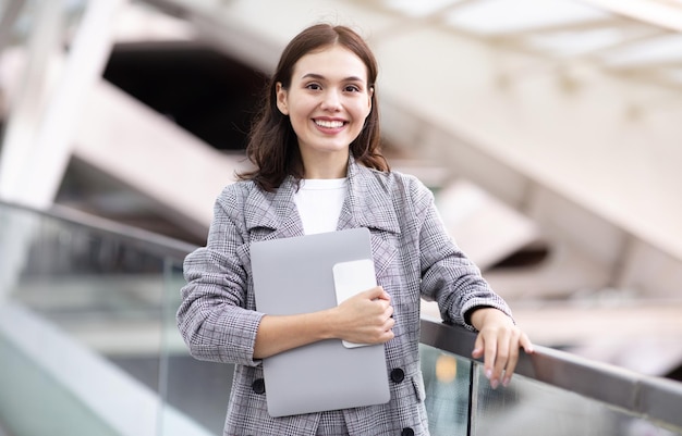 Happy young businesswoman holding laptop and smartphone at modern airport