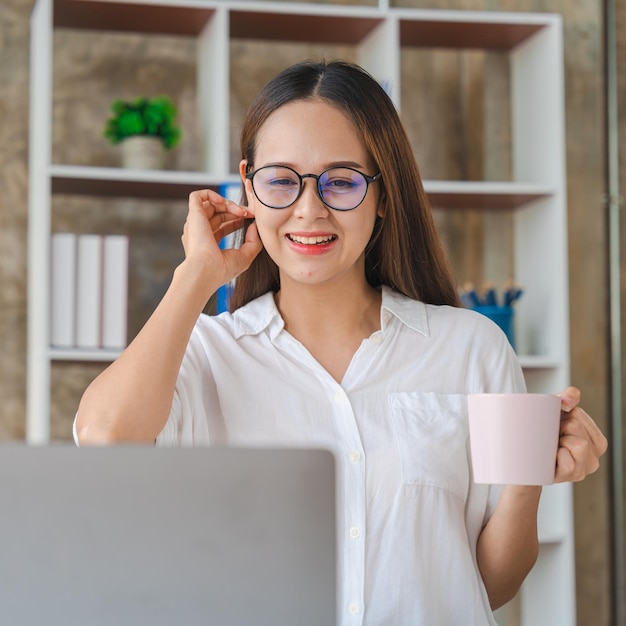 Happy young businesswoman using laptop computer doing online shopping Smiling beautiful Asian woman sitting and working at workplace