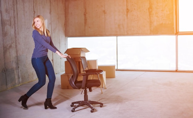 happy young casual business woman pushing office chair with sunlight through the windows during moving in at new unfinished startup office building