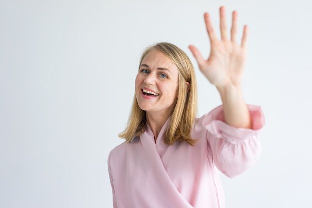 happy young Caucasian businesswoman wearing pink blouse waving hand in greeting