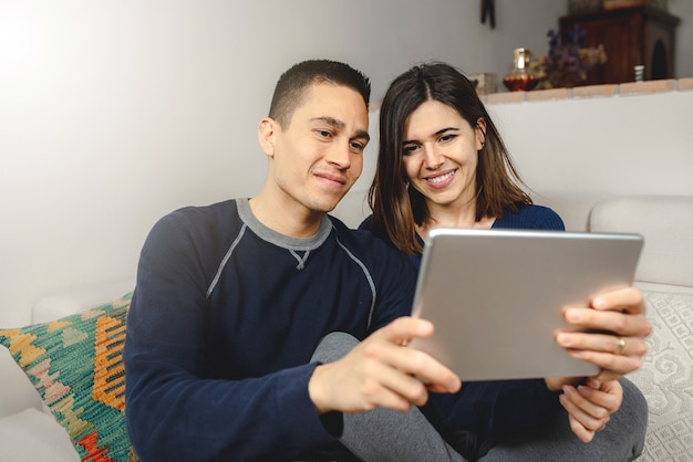 Happy young caucasian couple using laptop for a video call. talking and smiling sitting on the sofa at home.