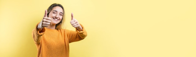 Happy young caucasian female in an orange sweater making thumb up sign and smiling Good job