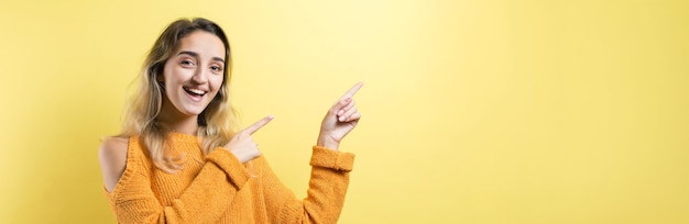 Happy young caucasian female in a yellow sweater pointing fingers away.