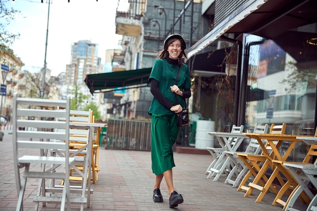 Happy young caucasian lady in green dress is walking near cozy cafe