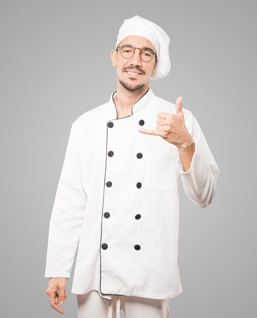 Happy young chef making a gesture of calling with the hand