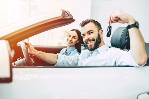 Happy young couple chooses and buying a new car for the family in the dealership