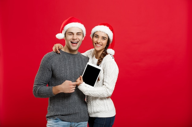 Happy young couple in christmas sweaters holding digital tablet.