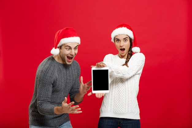 Happy young couple in christmas sweaters surprising something in digital tablet.