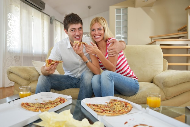 happy young couple eat fresh pizza at home relaxing and watch tv