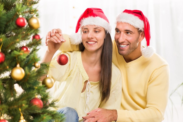 Happy young couple enjoy decorating Christmas tree at home.