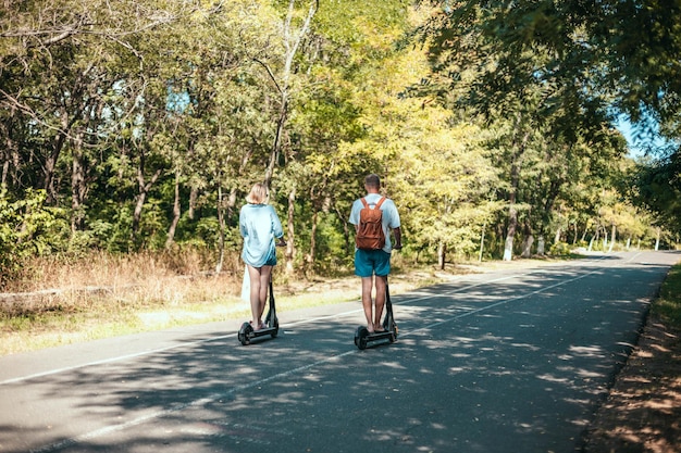 Happy young couple enjoying together while riding electric scooters in city park