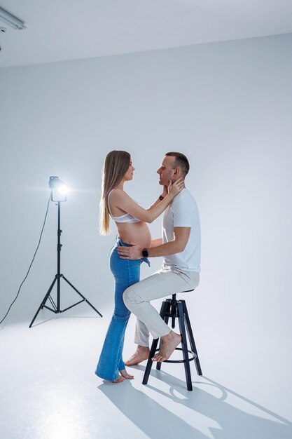 Happy young couple expecting a baby in white tshirts and jeans on a white background happiness of pregnancy and childbirth A happy married couple is expecting a child